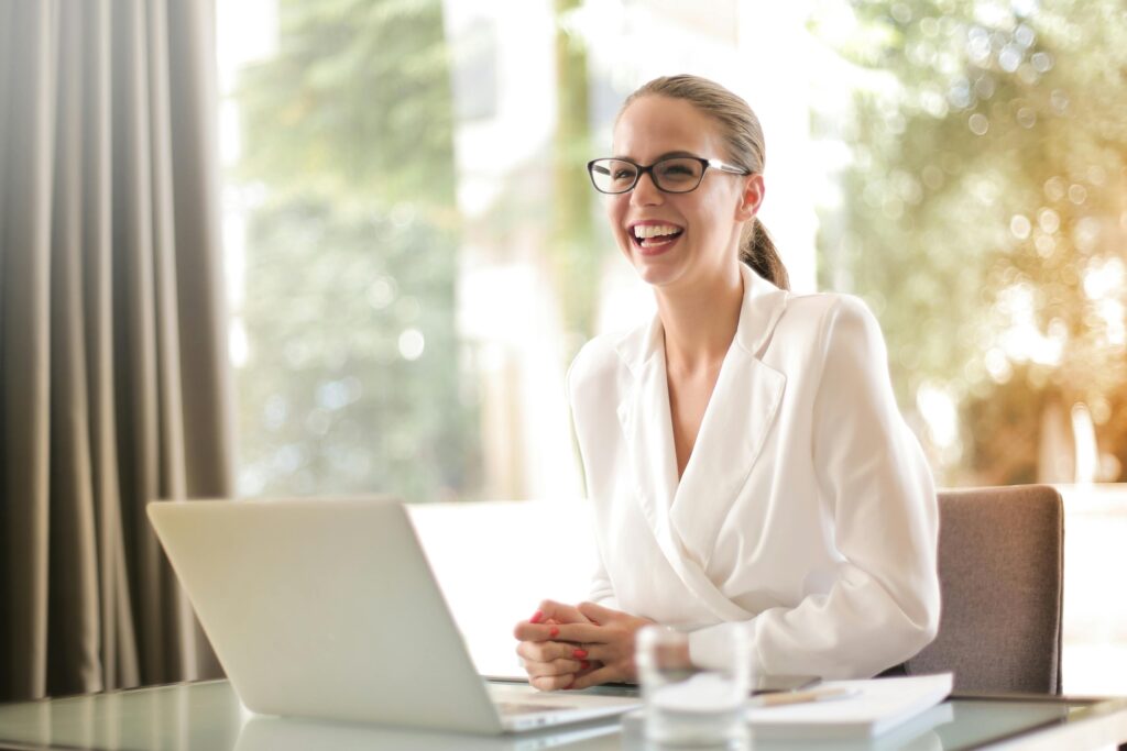 Young woman wearing eye glasses, working with a laptop while smiling happily