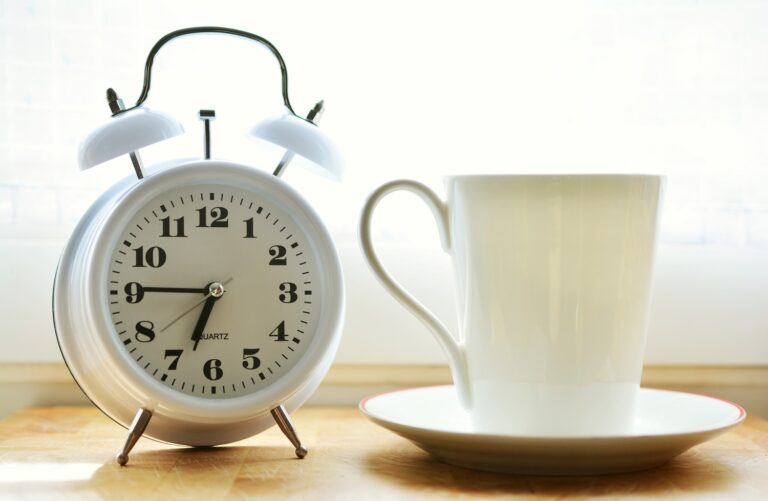 White alarm clock next to a white coffee cup and saucer