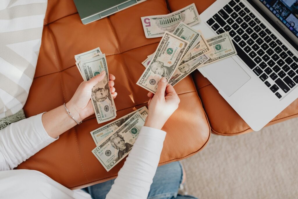 Woman counting dollar bills with a laptop in front of her